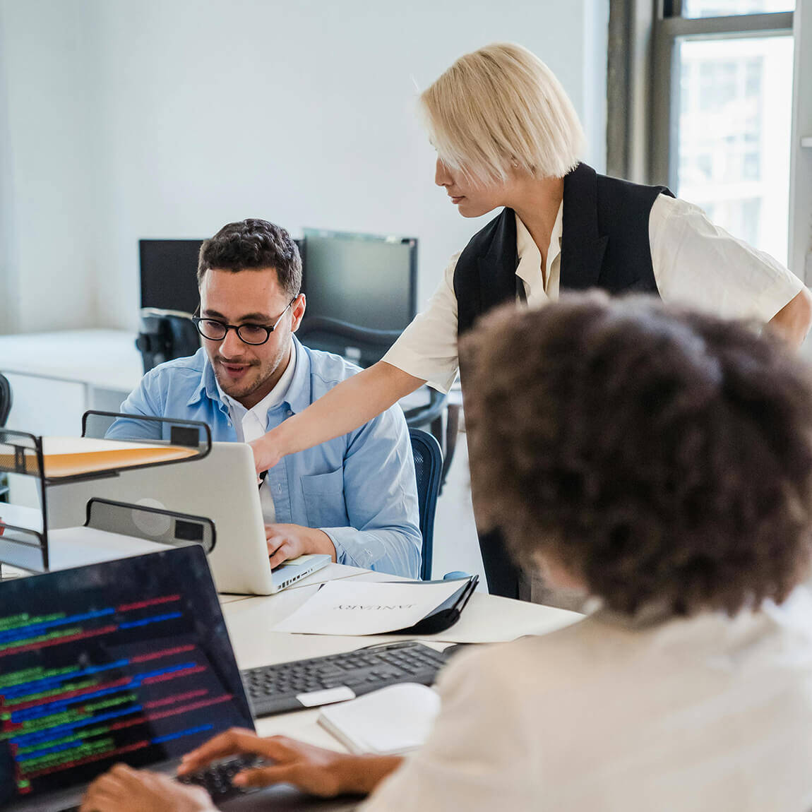 Collaborazione tra colleghi in ufficio che analizzano righe di codice software su un monitor