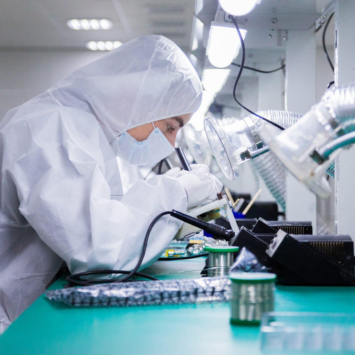 Operatore in tuta protettiva sterile mentre lavora su componenti elettronici in camera bianca